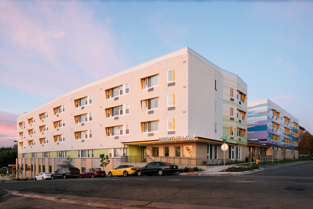 Arroyo Village building at sunset with colorful exterior and parked cars in front