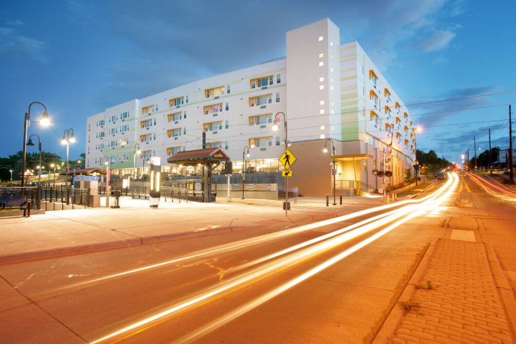 Modern six-story apartment building illuminated at dusk, with car light trails on the street, enhancing urban ambiance.