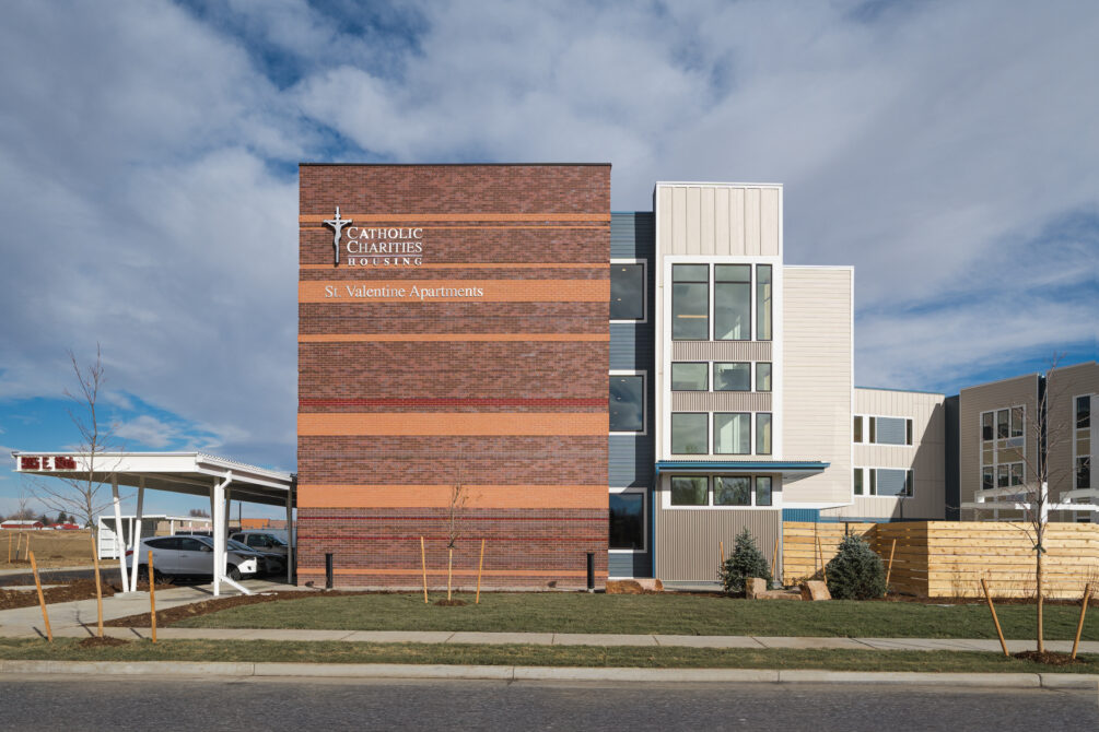 St. Valentine Apartments building with "Catholic Charities Housing" text on brick facade under cloudy sky