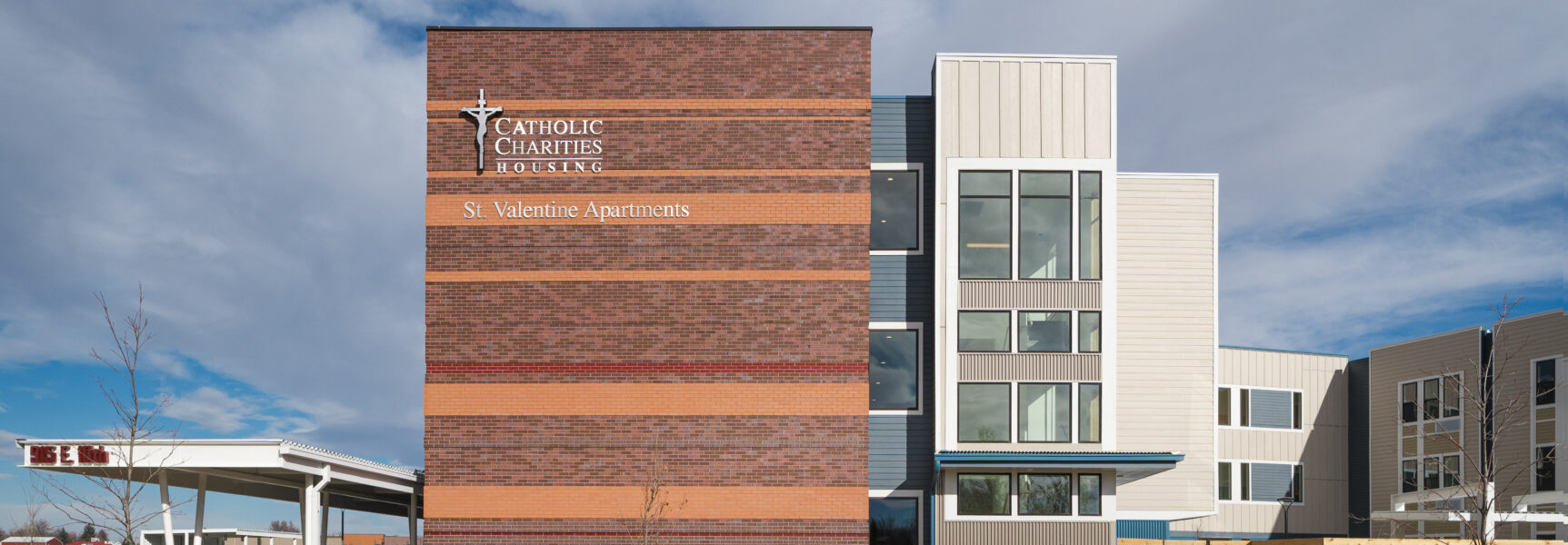 St. Valentine Apartments exterior with "Catholic Charities Housing" sign on brick facade.