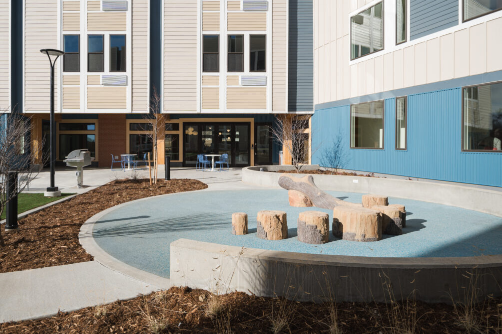 Courtyard with log seating, modern building exterior, and outdoor tables and chairs