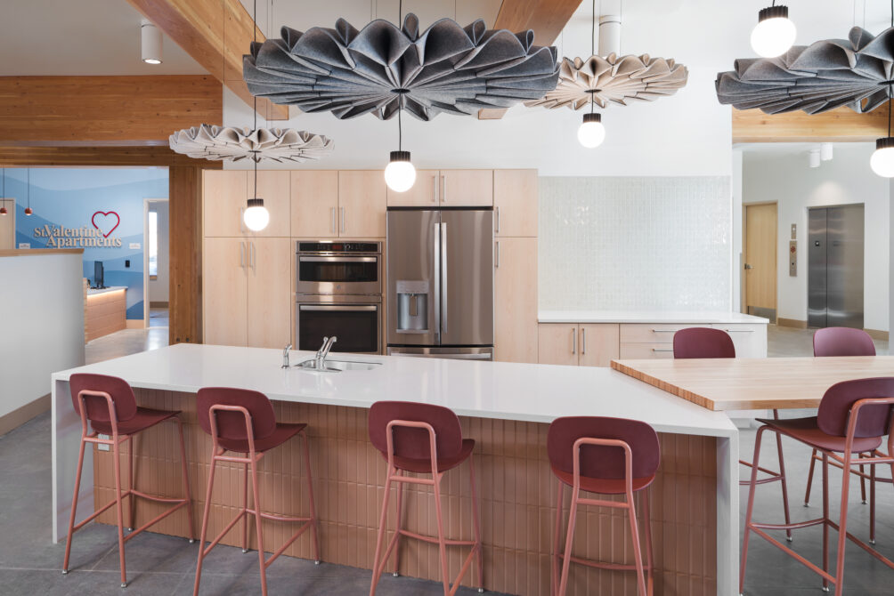 Modern kitchen with white countertops, maroon chairs, unique ceiling lights. "St. Valentine Apartments" logo on blue wall.