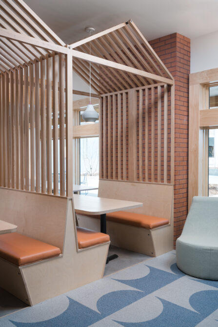 Modern lobby seating with wooden partitions, orange cushions, geometric carpet, and pendant lighting.