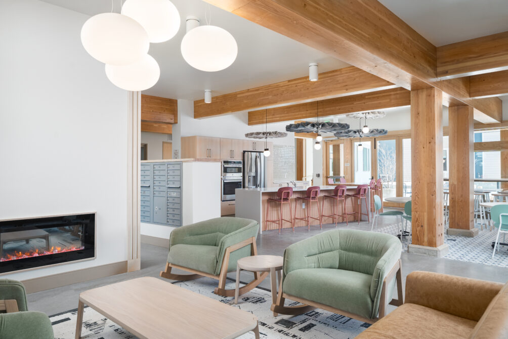 Modern lobby with green armchairs, wood beams, and a cozy fireplace; communal kitchen area with bar stools