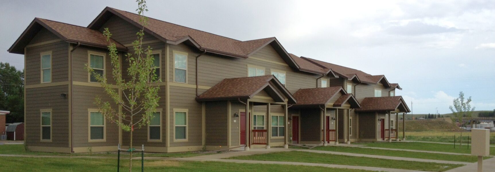 Brown townhouse complex with green lawn and young trees.