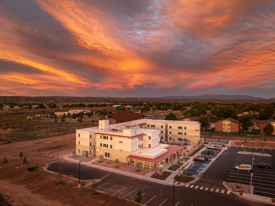 Building surrounded by parking lot at sunset with dramatic orange sky.