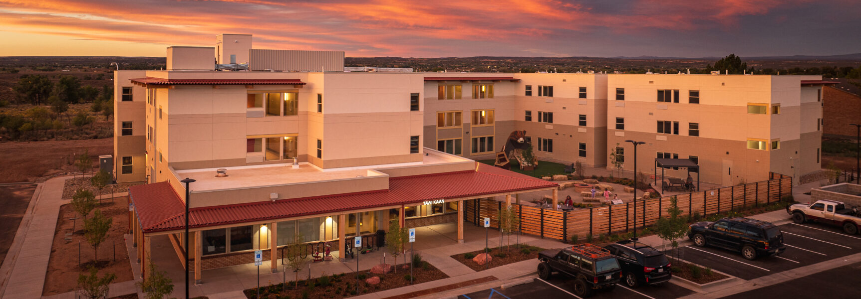 Tawi Kaan facility at sunset with a courtyard and parked cars.