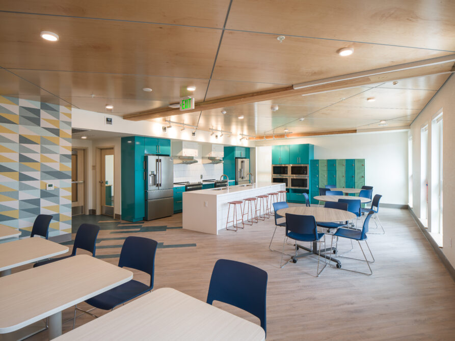 Modern communal kitchen with teal cabinets, dining tables, and colorful geometric wall tiles
