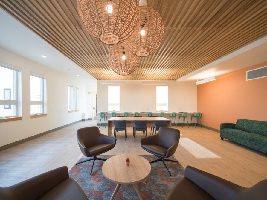 Modern lounge area with woven light fixtures, armchairs, long table, and windows.