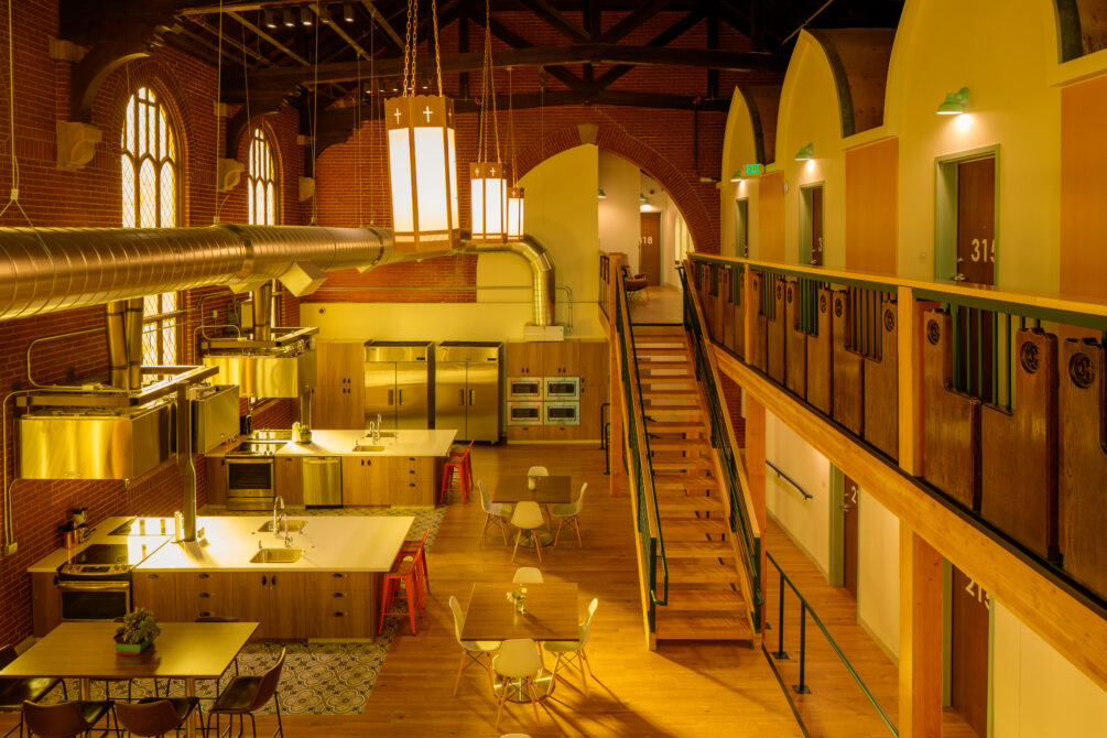 Warmly lit communal kitchen area inside Warren Residences with modern fixtures, large tables, and industrial details.