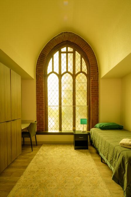 Bright room with arched window, single bed, desk, and wardrobe.