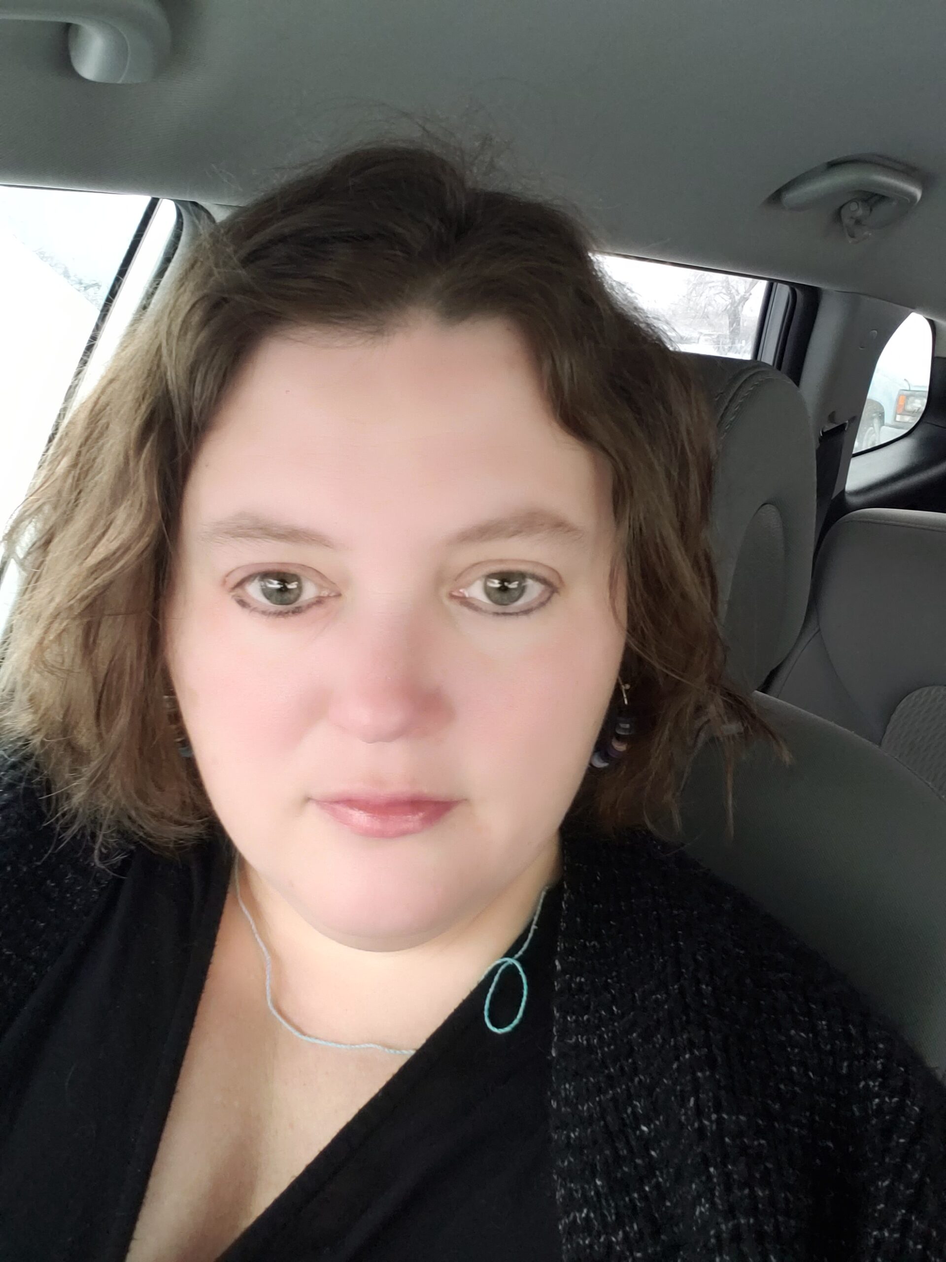 Brooke sitting in a car, wearing a black sweater, neutral expression.