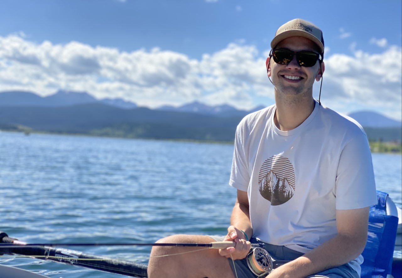 Cameron smiling while fishing on a lake, mountains in background