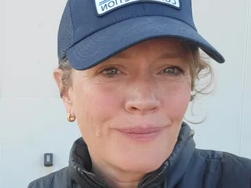 Erin wearing a blue baseball cap, smiling softly outdoors.