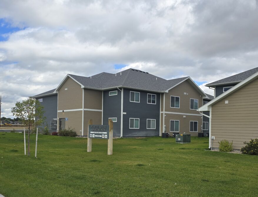 Platte River Apartments sign on grass, beside modern apartments under cloudy sky.