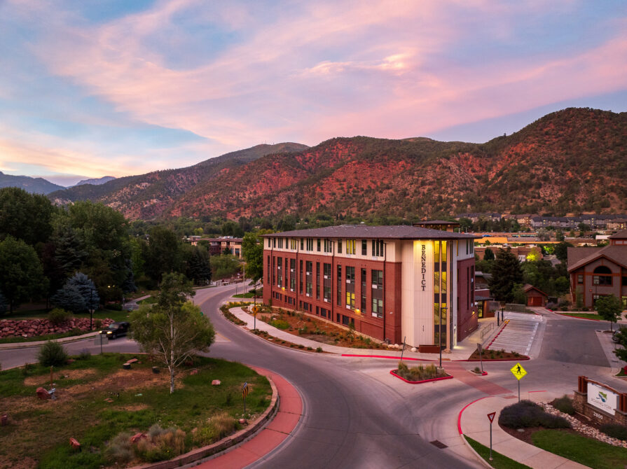 Benedict building amid scenic mountainous landscape during sunset, with winding road and lush greenery surrounding it