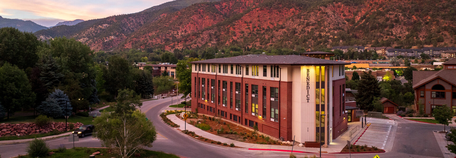 Benedict building at sunset, surrounded by greenery and mountains