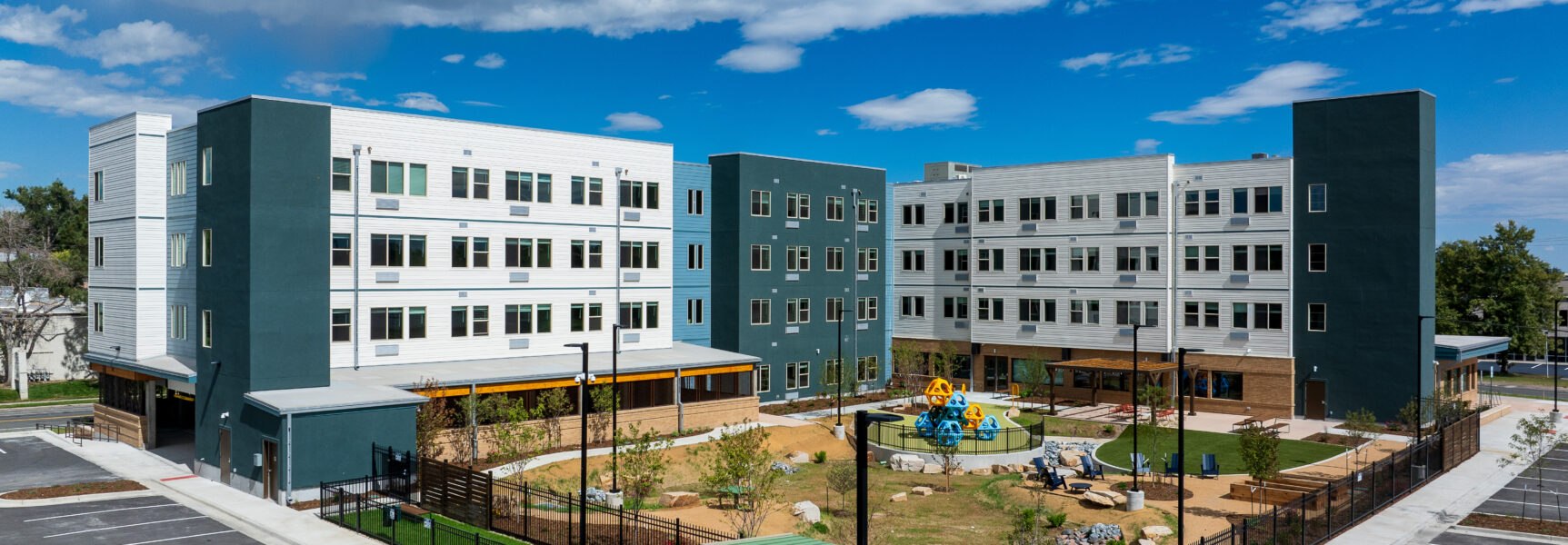 Modern apartment complex with adjacent playground and landscaped courtyard under a clear blue sky.