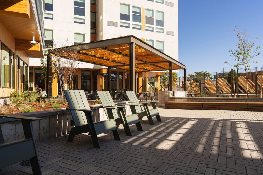 Outdoor patio with wooden pergola, green chairs, and modern building backdrop