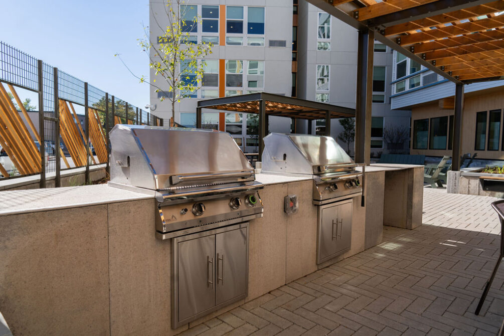Outdoor patio with two stainless steel grills, shaded by a wooden pergola.