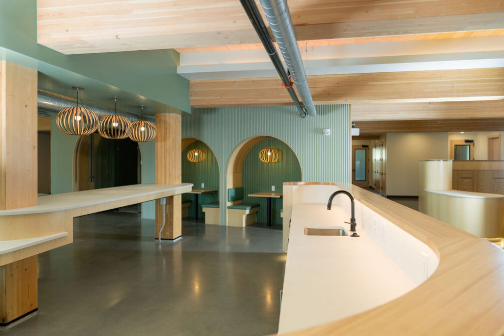 Modern interior with wooden arches, green booths, and pendant lights over a curved countertop sink area