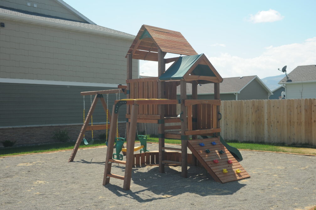 Playground set with swings, slide, and climbing wall in fenced yard