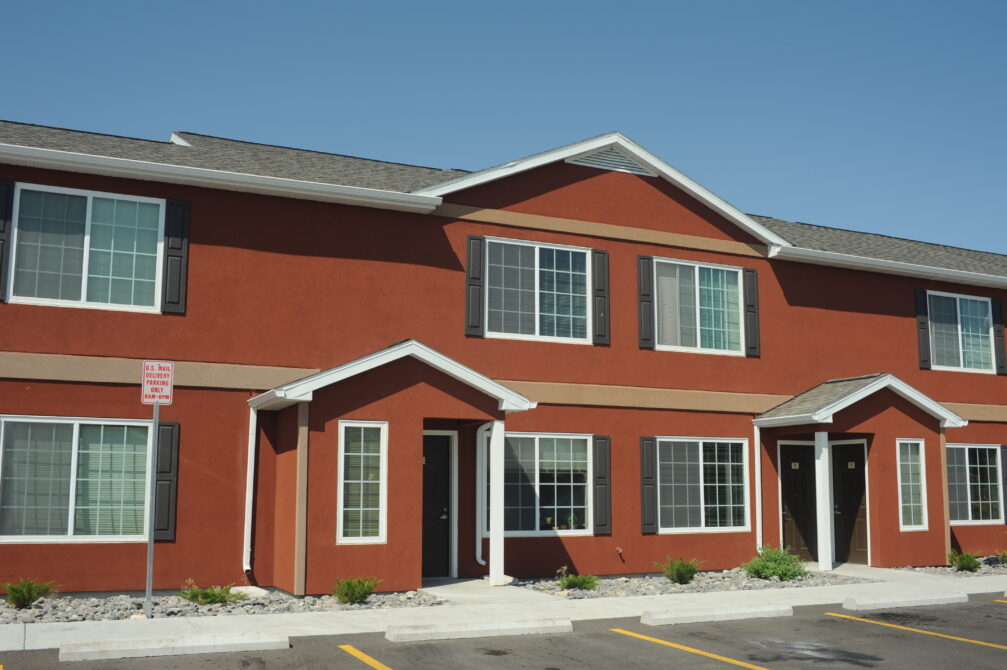 Red two-story townhouse with white trim, large windows, and parking signs in front.