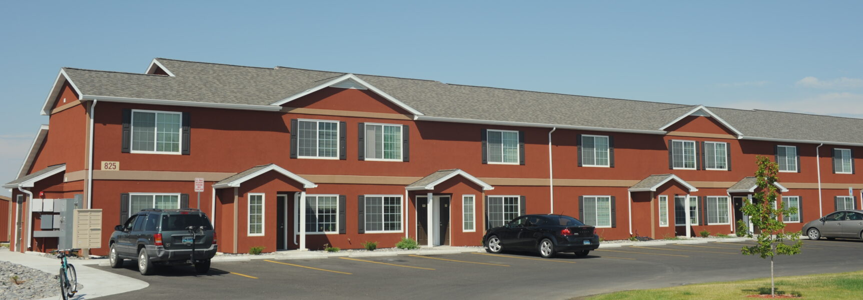 Red two-story building with multiple units, parking spaces, and a bicycle. Address number "825" displayed.