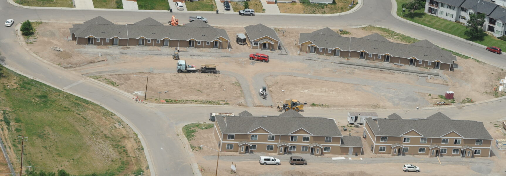 Aerial view of a residential construction site with multiple brown buildings, vehicles, and partially completed landscaping.