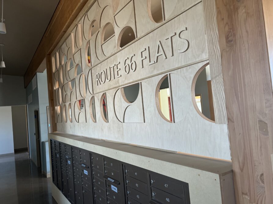 Wooden wall with cutouts reading "ROUTE 66 FLATS" above mailboxes in hallway