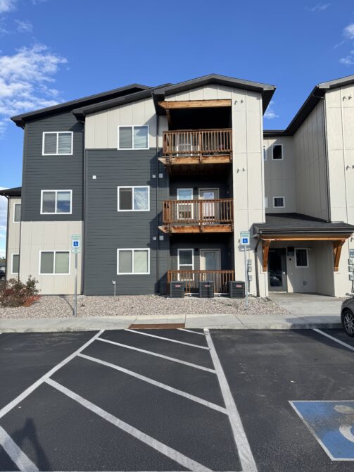 Three-story apartment building with wooden balconies and accessible parking spaces.
