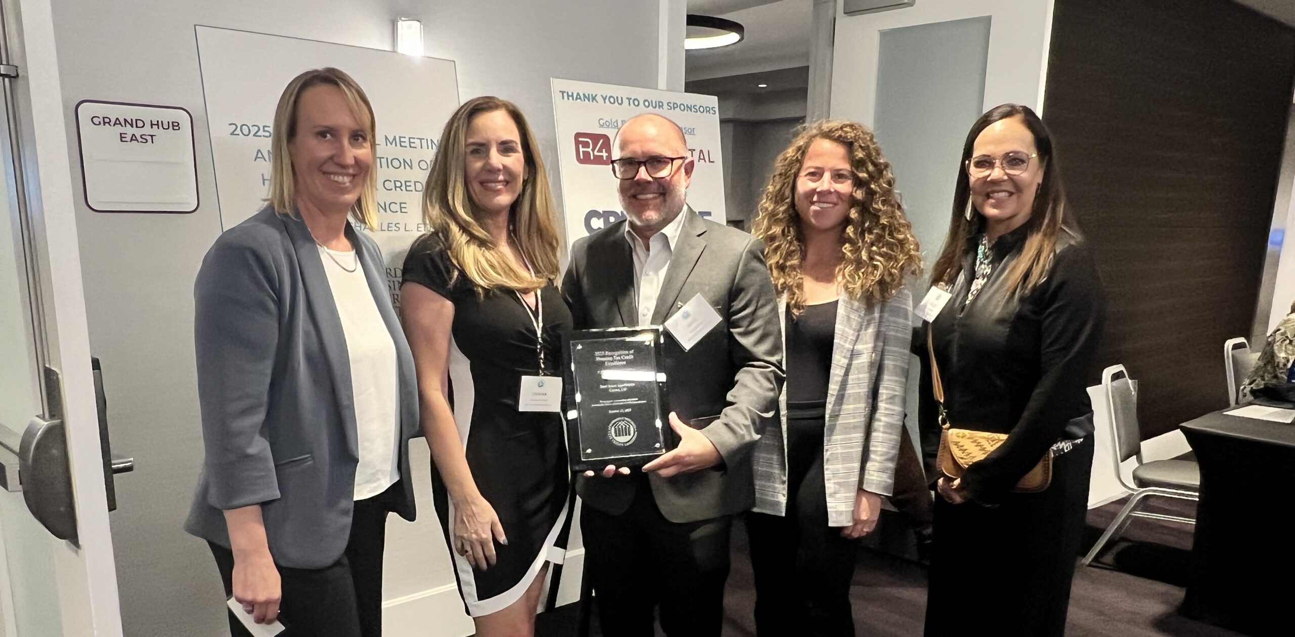 Five people smiling, two holding an award, indoors at a conference.