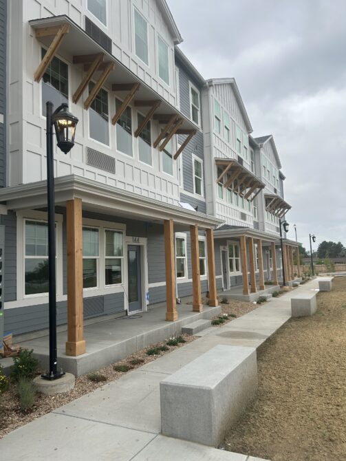 Modern three-story building with wooden accents, lined windows, and a front pathway under a cloudy sky.