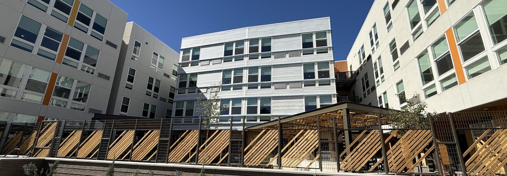 Contemporary multi-story apartment complex with geometric facade and courtyard under clear blue sky