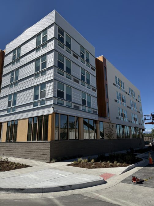 Modern multi-story building with large windows, white and brown facade, on a sunny day.