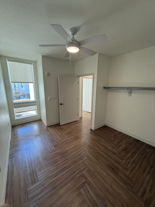 Empty room with parquet flooring, a ceiling fan, and a window with a blind partially down, next to an open door
