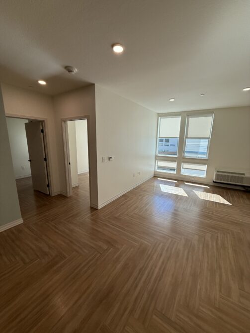 Empty room with wooden floors, two doorways, large windows, and natural light filling the space