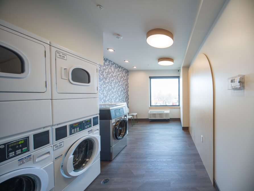 Modern laundry room with stacked washers, dryers, and patterned wallpaper.