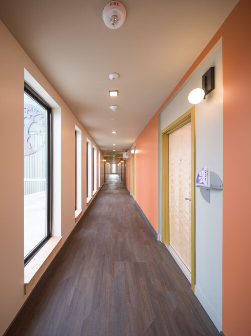 Long corridor with warm peach walls, large windows, and a door labeled "2021."