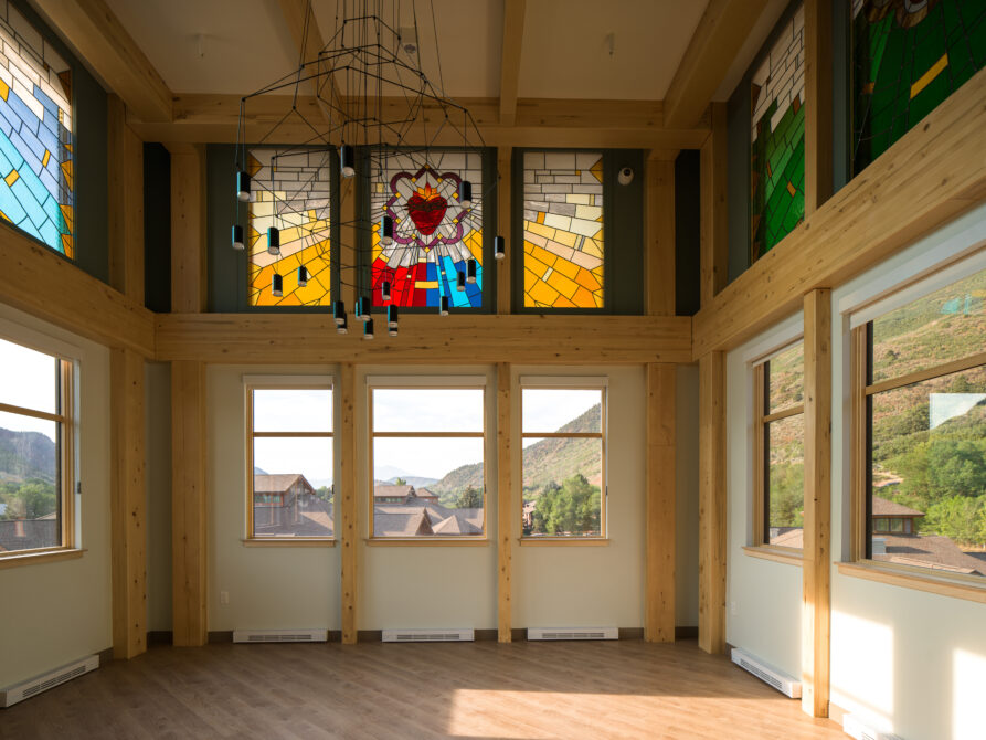 Sunlit room with large stained glass window featuring a vibrant Sacred Heart design and wooden beams.