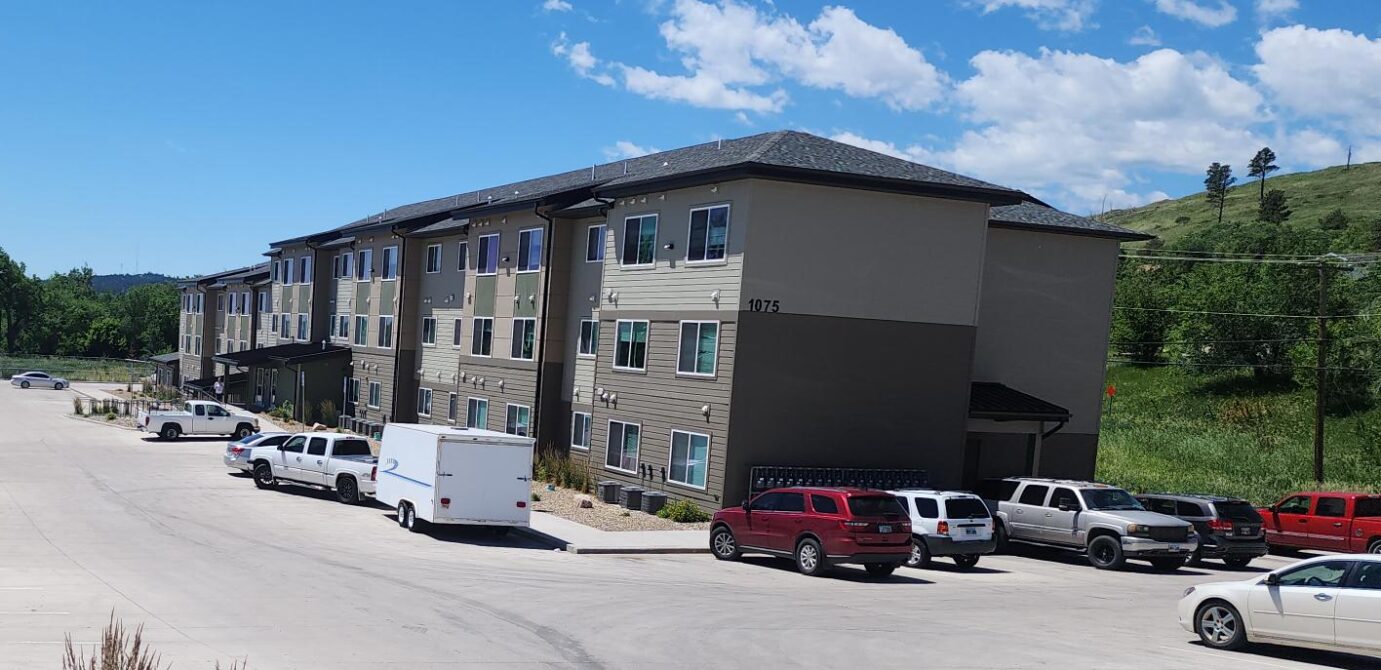 Three-story beige building at 1075 with parked vehicles in lot, surrounding greenery