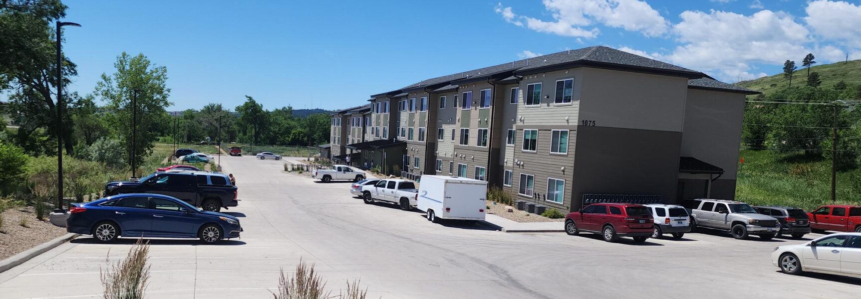 Three-story building labeled 1075 with cars parked in the lot, surrounded by greenery.