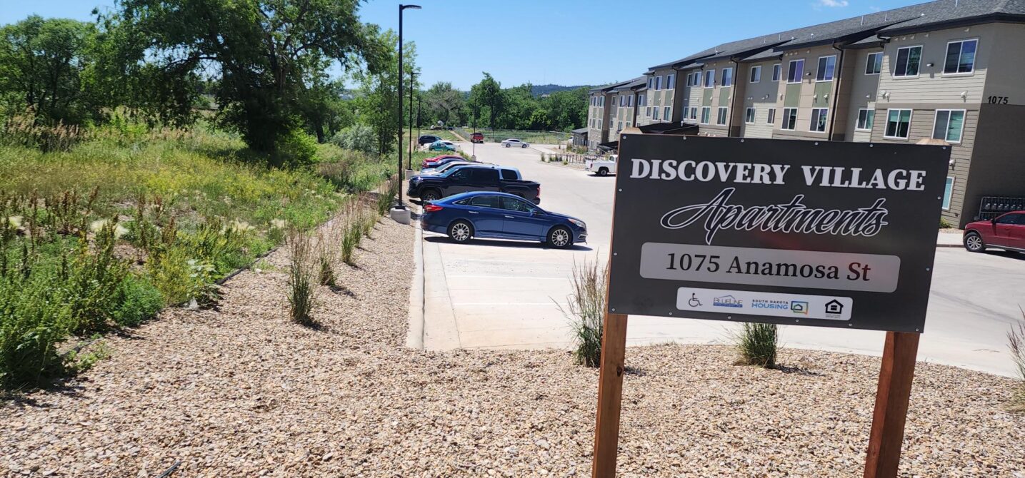 Discovery Village Apartments sign at 1075 Anamosa St, near parking area and greenery.