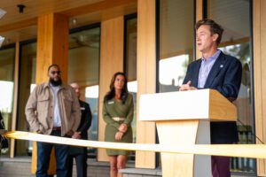 Man speaking at podium during ribbon-cutting ceremony, with attendees watching