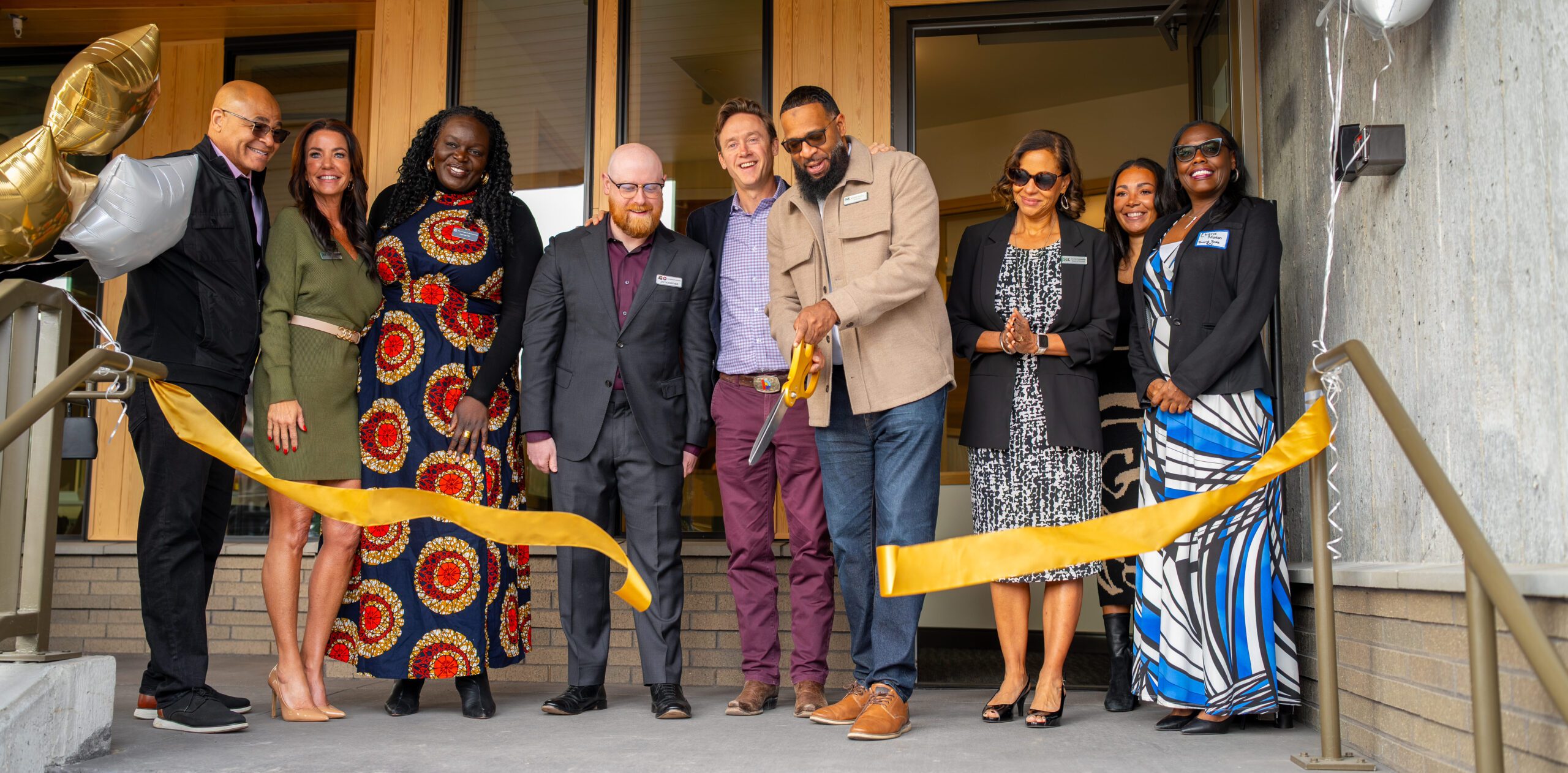 Group gathered for ribbon-cutting ceremony; individual cutting ribbon with large scissors