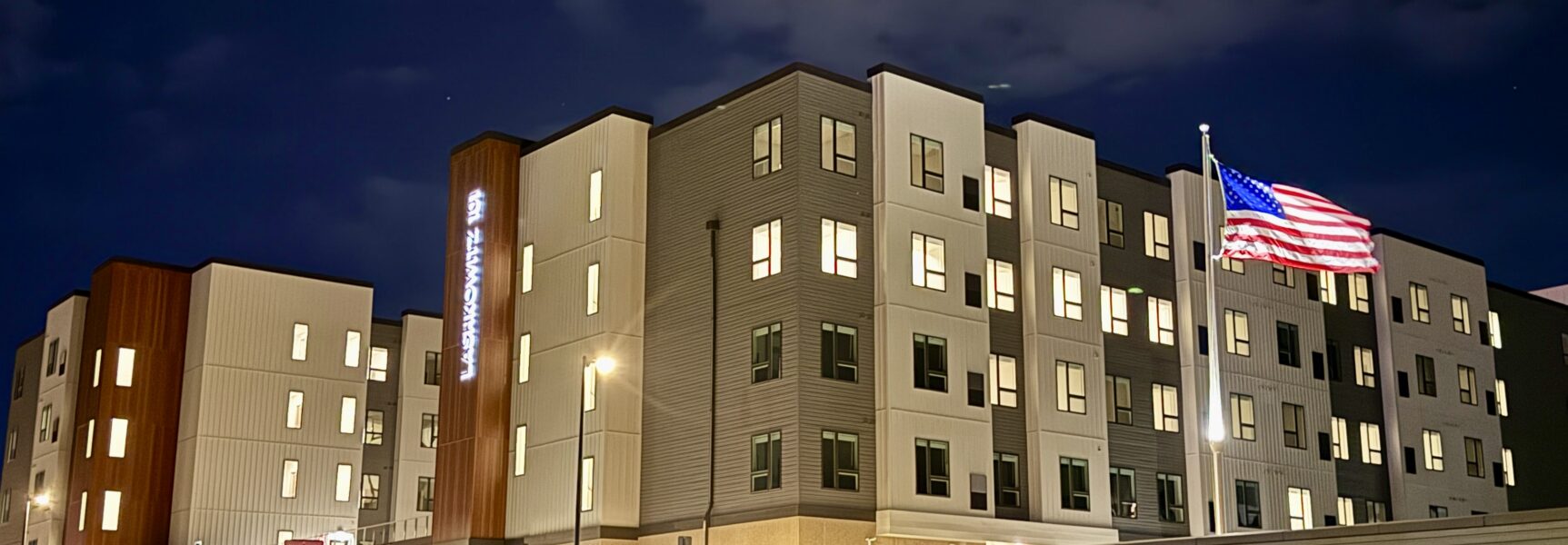 Modern apartment building lit at night with American flag.