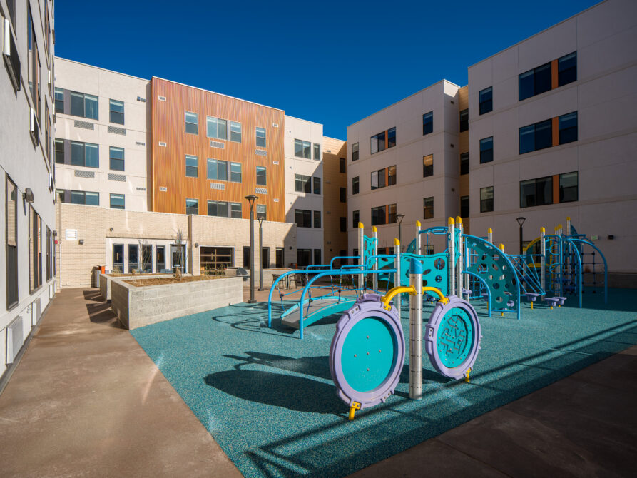 Colorful playground in an apartment complex courtyard, surrounded by modern buildings under a clear blue sky.