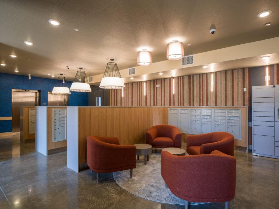 Lobby with red armchairs, circular tables, pendant lights, mailboxes, and striped wallpaper.